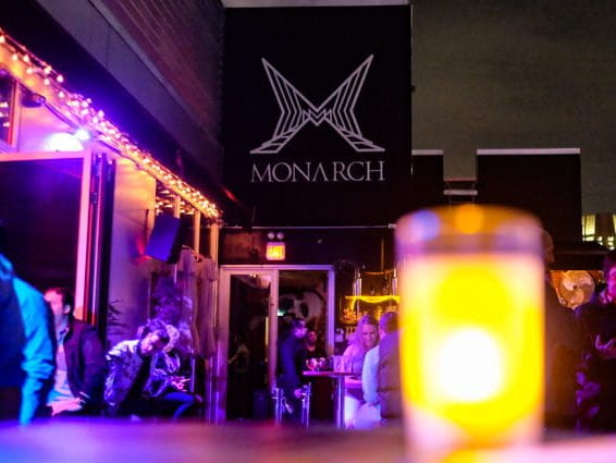 Candle on table with people and Monarch logo in background